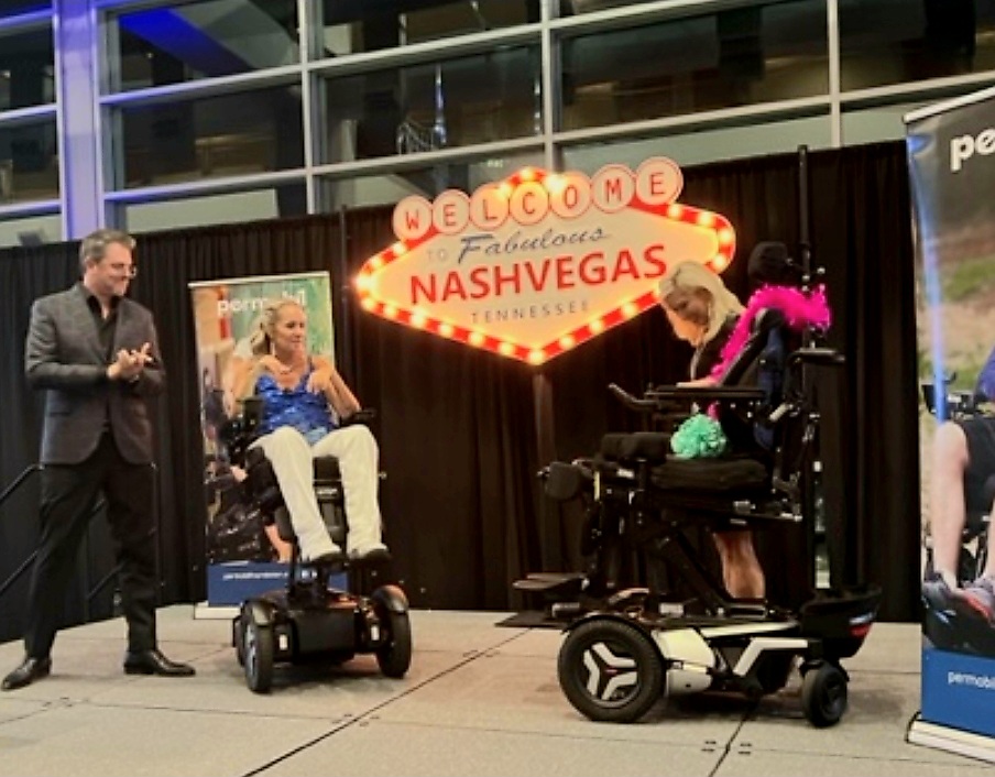 image of Ali and wheelchair on stage being presented new wheelchair
